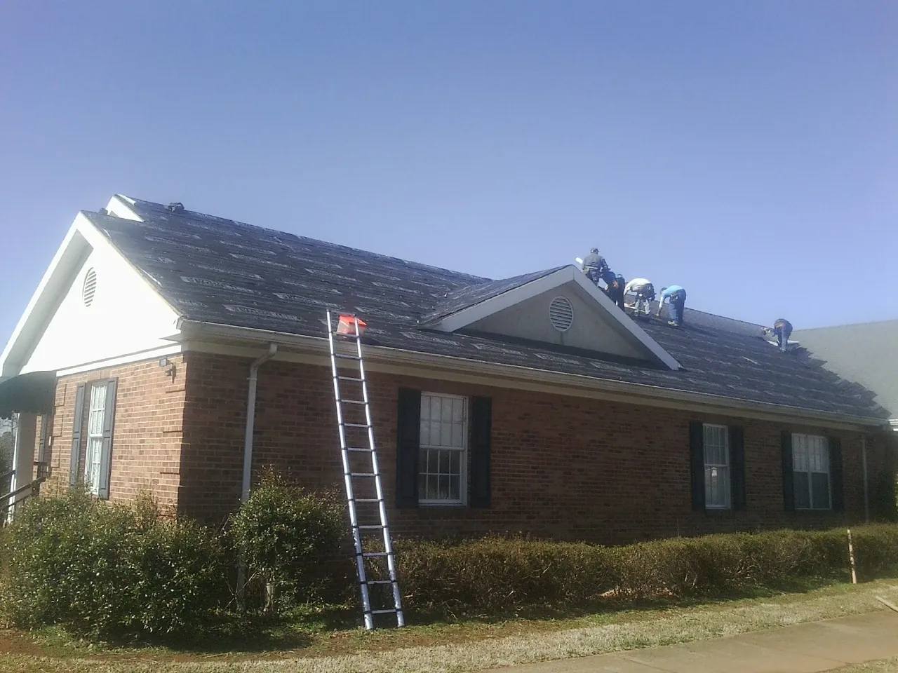 Crew tearing shingles off a brick ranch roof with a ladder set — Metal Roof Repair work by our crew in La Plume
