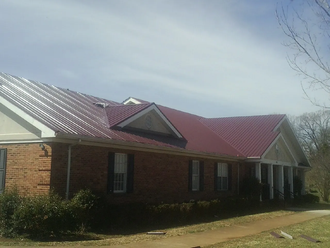 Red metal roof with gabled entries on a long brick building, from a Hail Damage Roof Repair job in La Plume