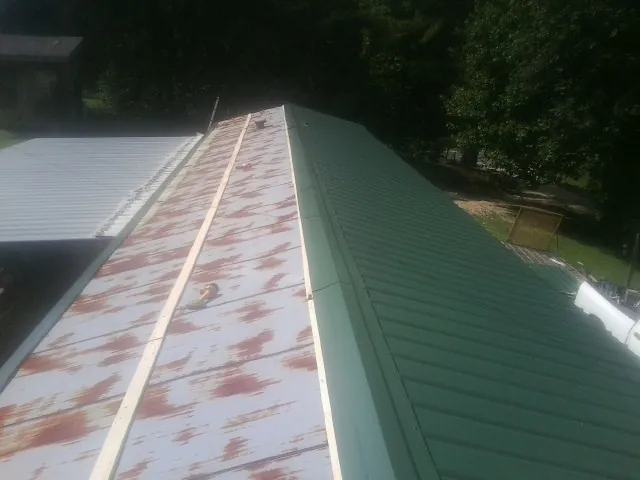 Old rusted panels beside newly installed green metal roofing — Wind Damage Roof Repair by Roofing Brothers in La Plume