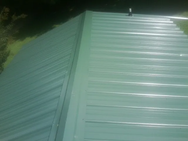 New green metal panels meeting at the ridge of a roof — Flat Roof Repair work by our crew in La Plume