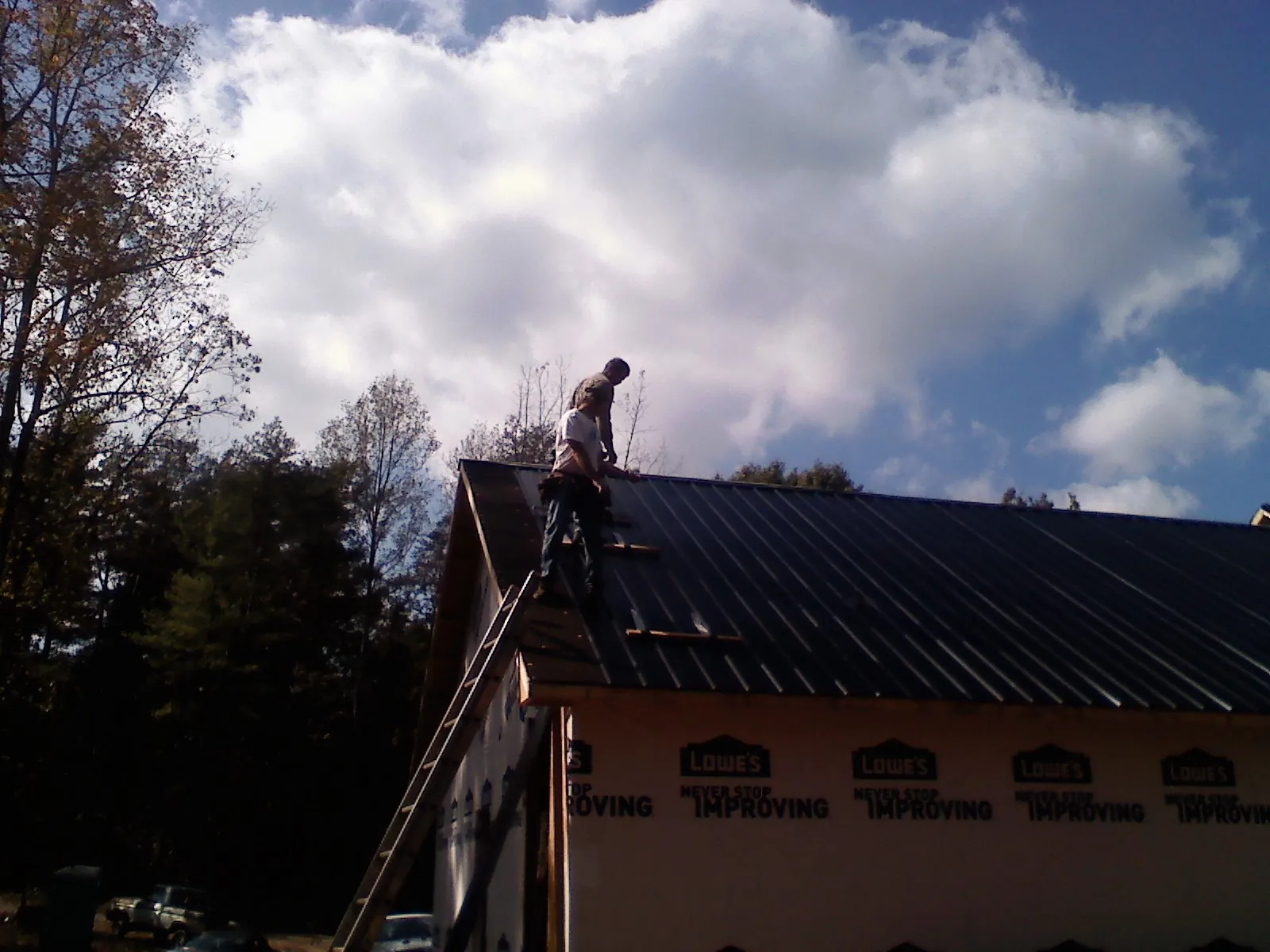 Roofer fastening dark metal panels high against a cloudy sky, from a Roof Inspection job in La Plume