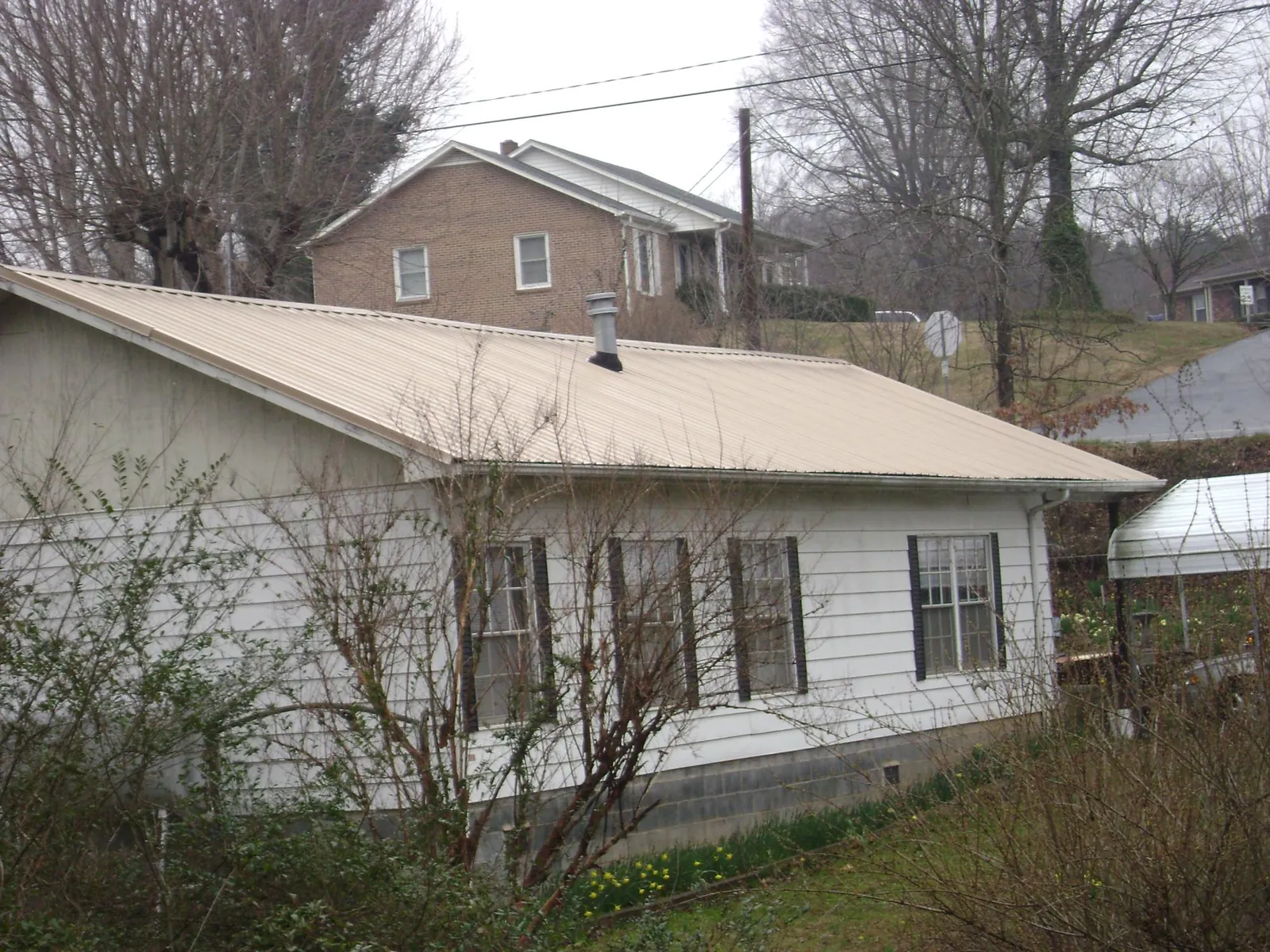 Tan metal roof on a white sided house set into a hillside — Commercial Roofing by Roofing Brothers in La Plume