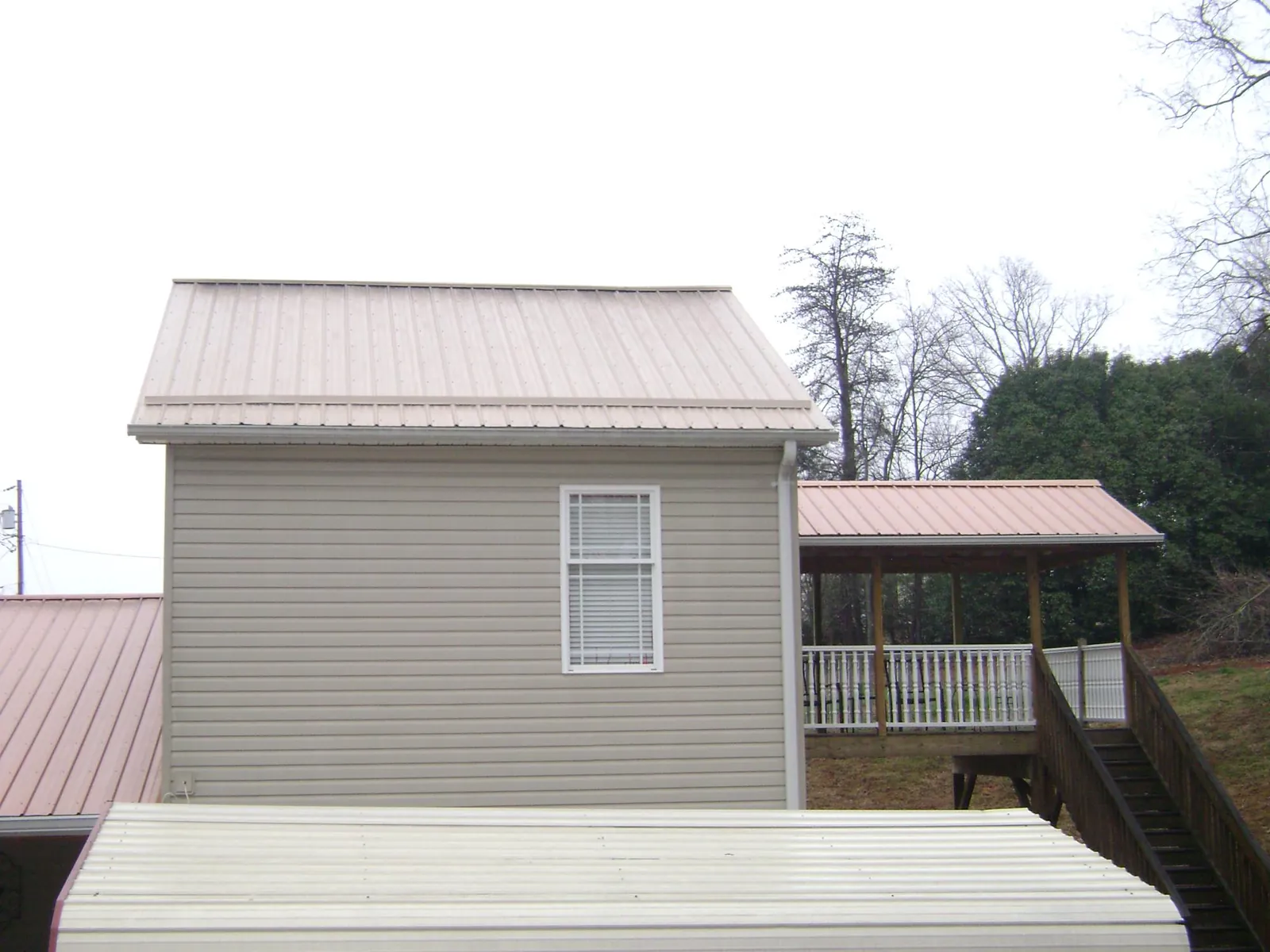 Tan metal roofs on a two story addition and attached porch, from a Roof Replacement job in La Plume